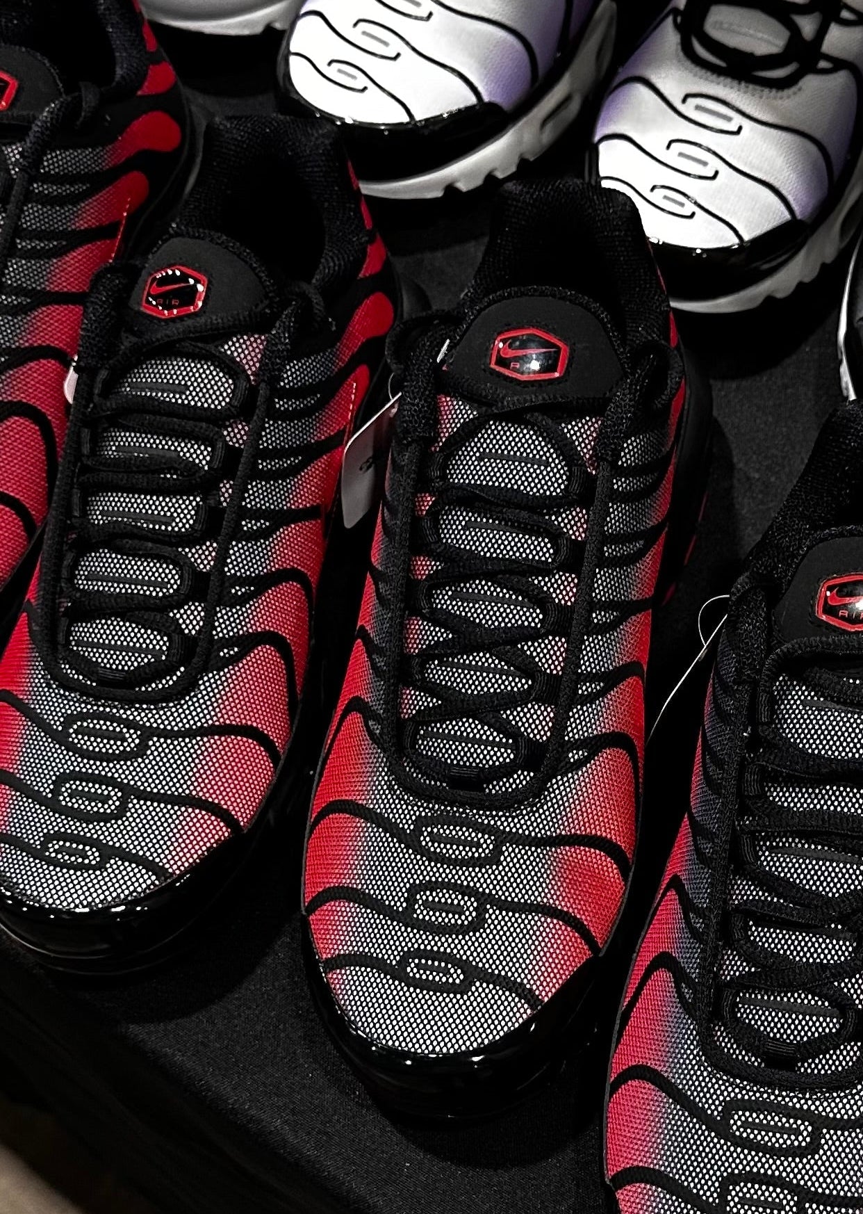 Close-up of black and red sneakers with a brand logo on a dark surface.